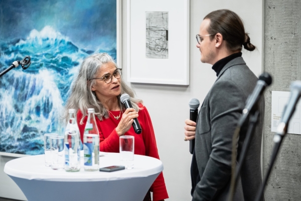 Natascha Euteneier im Kunst-Gespräch mit Benedikt Walther. Im Hintergrund ein gischtendes Blau von Heidi Hahn und ein schwarzweißes Blatt von Andreas Böhm.